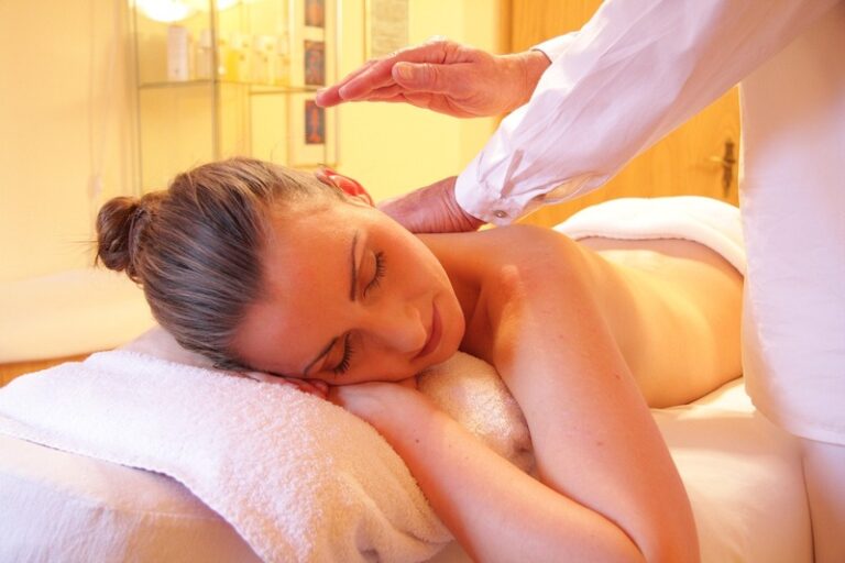 Une personne reçoit un massage apaisant du dos alors qu'elle est allongée sur une serviette blanche, tandis que les mains expertes de la masseuse appuient avec expertise sur son cou, en utilisant une technique anti-cellulite pour une relaxation accrue.